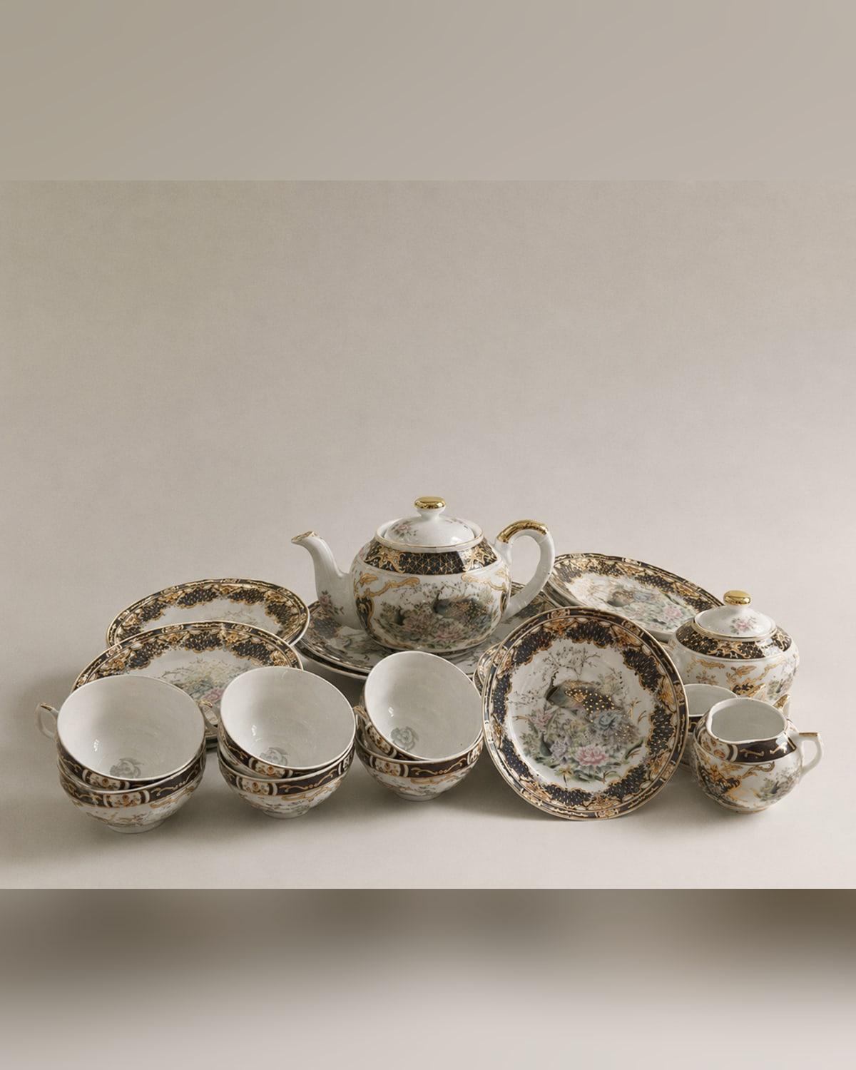 A full porcelain tea service in navy and gold, each piece painted with a peacock among peonies and blossom, teapot at the centre with stacked cups and plates around it.