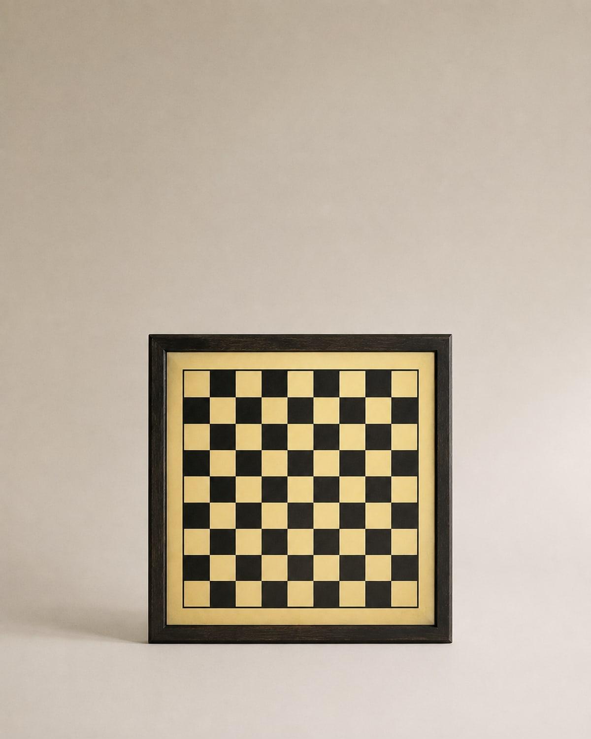A chess board standing upright in a dark timber frame, its sixty-four squares alternating matte black and pale straw yellow with a fine border line drawn around the playing area.