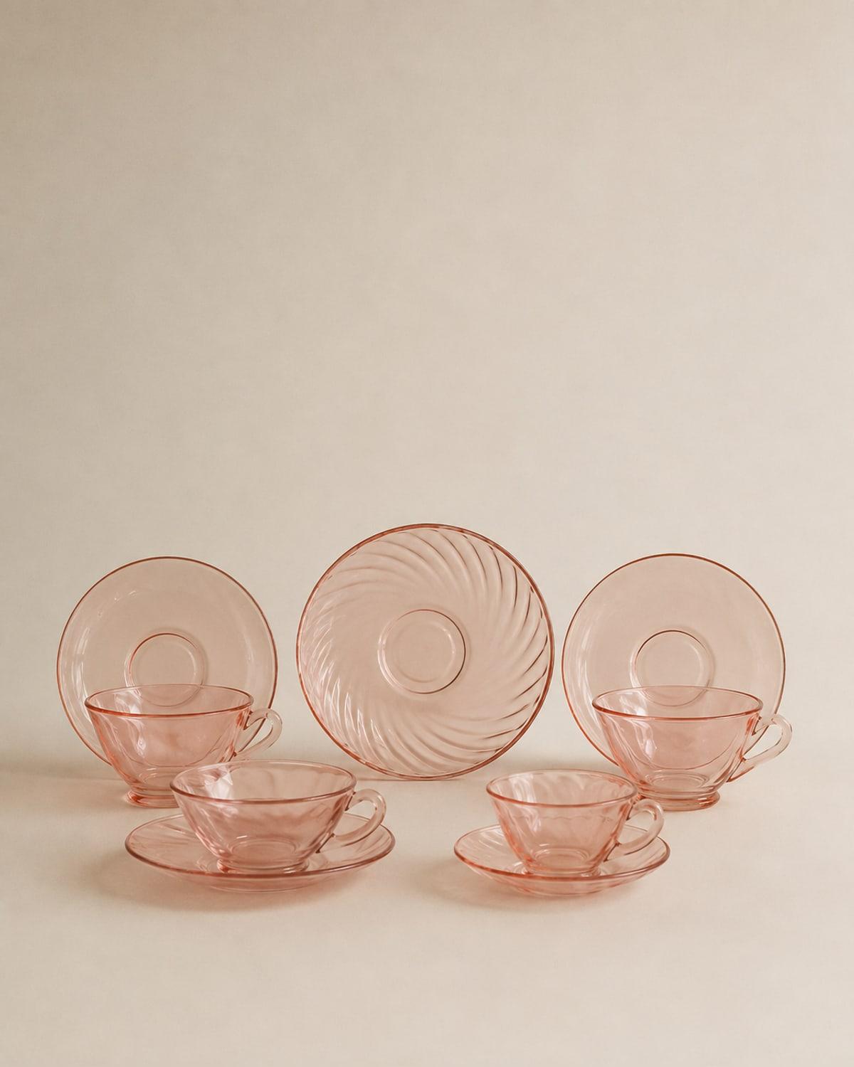 Four pink pressed-glass teacups with matching saucers, the glass a clear rose colour, one saucer stood upright to show a swirled fluting on its underside.