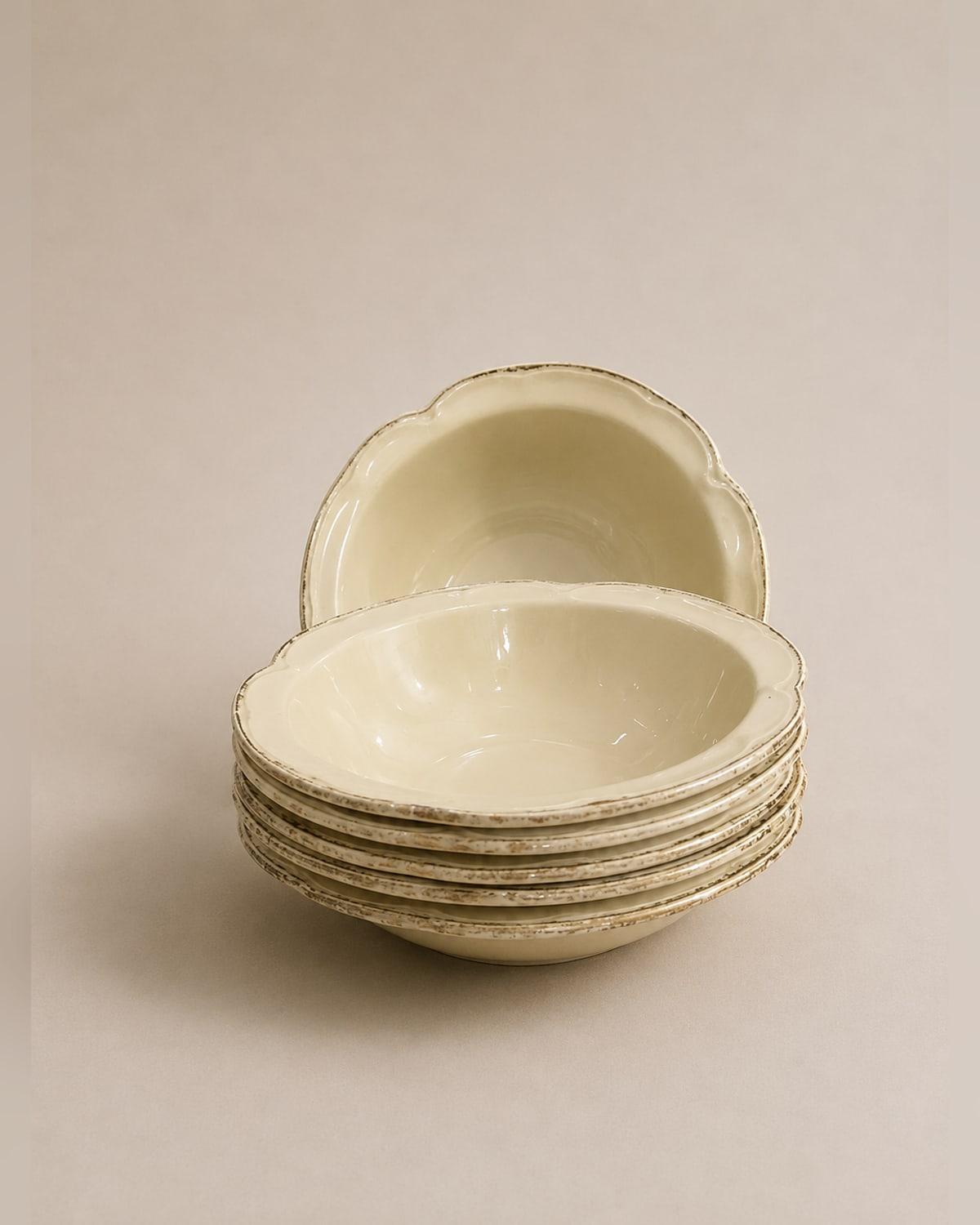 Six deep cream bowls with a scalloped edge stacked together, one propped upright behind, the rims flecked with brown where the glaze has worn.
